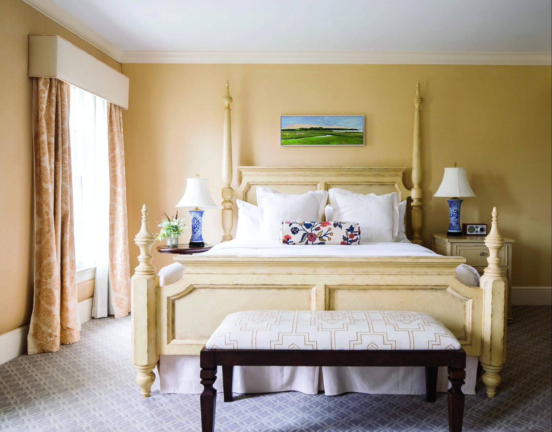 A wide view of a hotel room with a large bed, nightstands, and a bench at the foot of the bed.