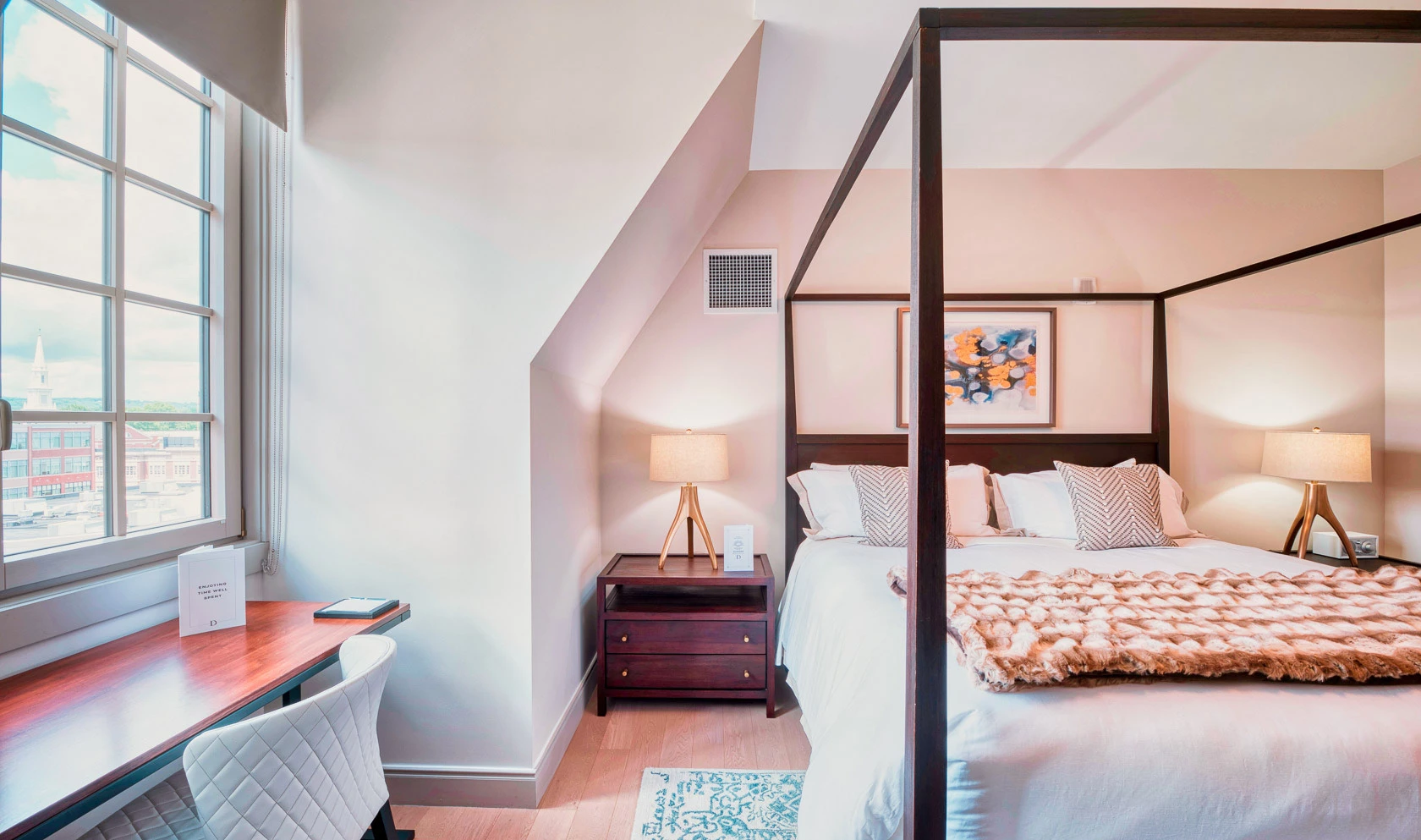 A clean and modern guest room with a four-poster bed, desk, and window