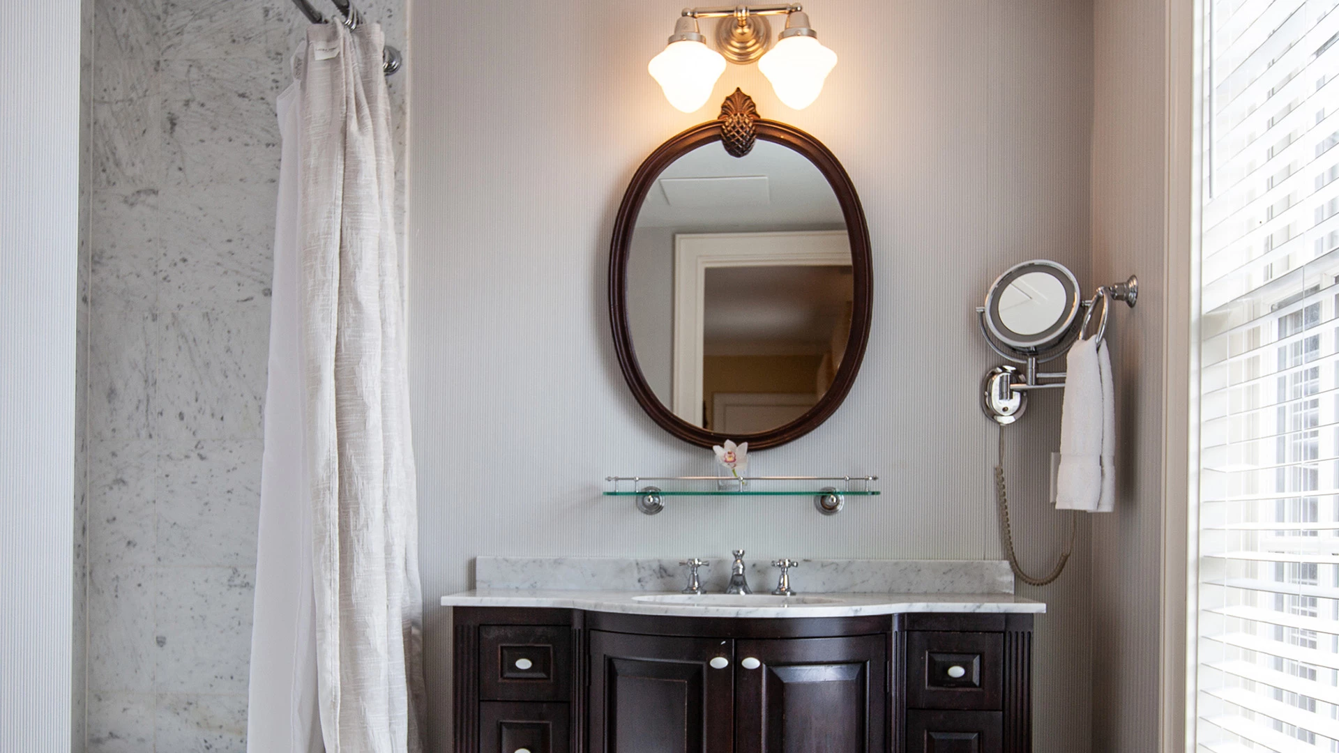 A bathroom vanity with a marble countertop, dark wood cabinets, and a large mirror above the sink.