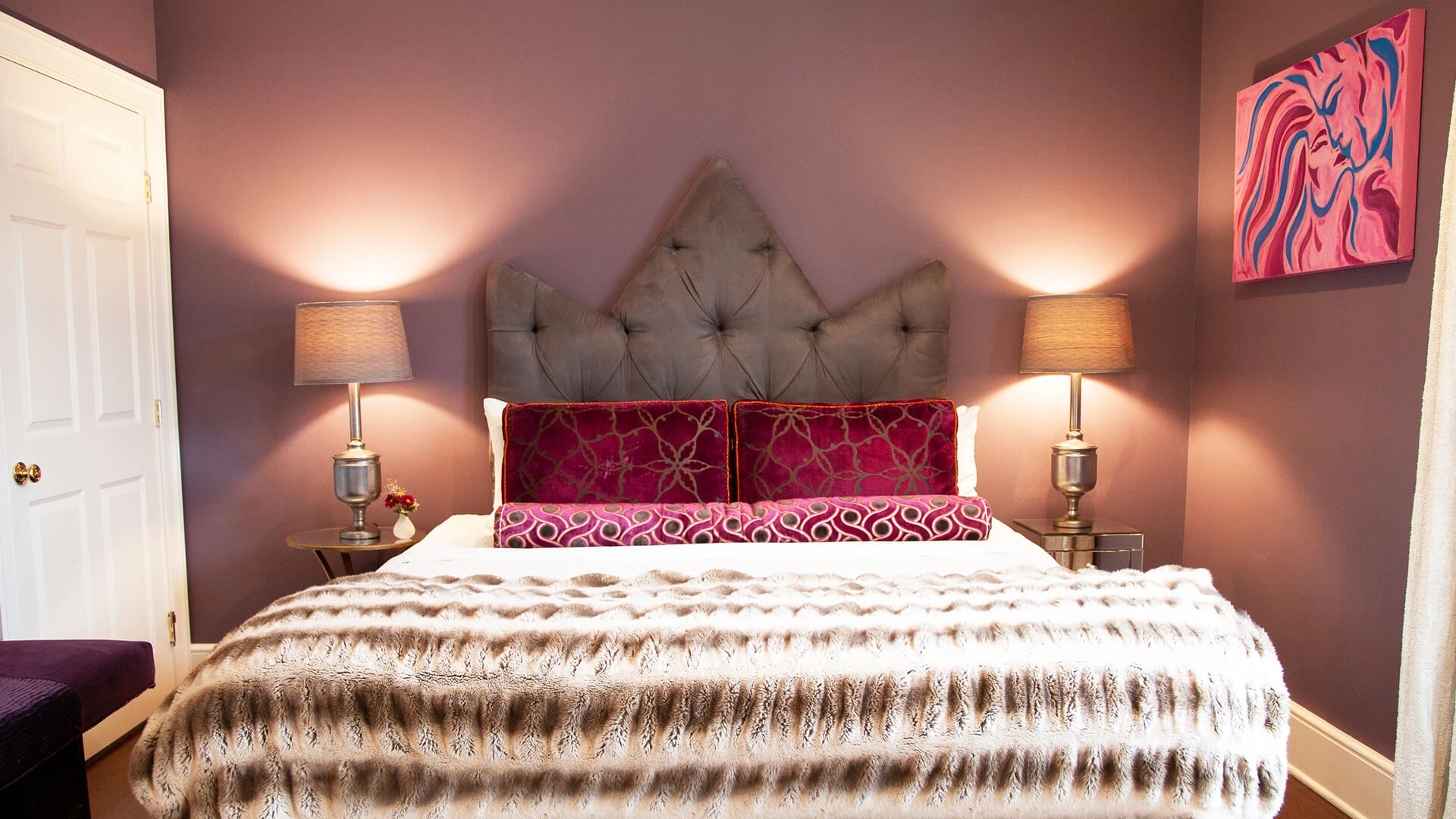 A bed with a tufted headboard, two lamps, and a piece of abstract artwork on the wall.