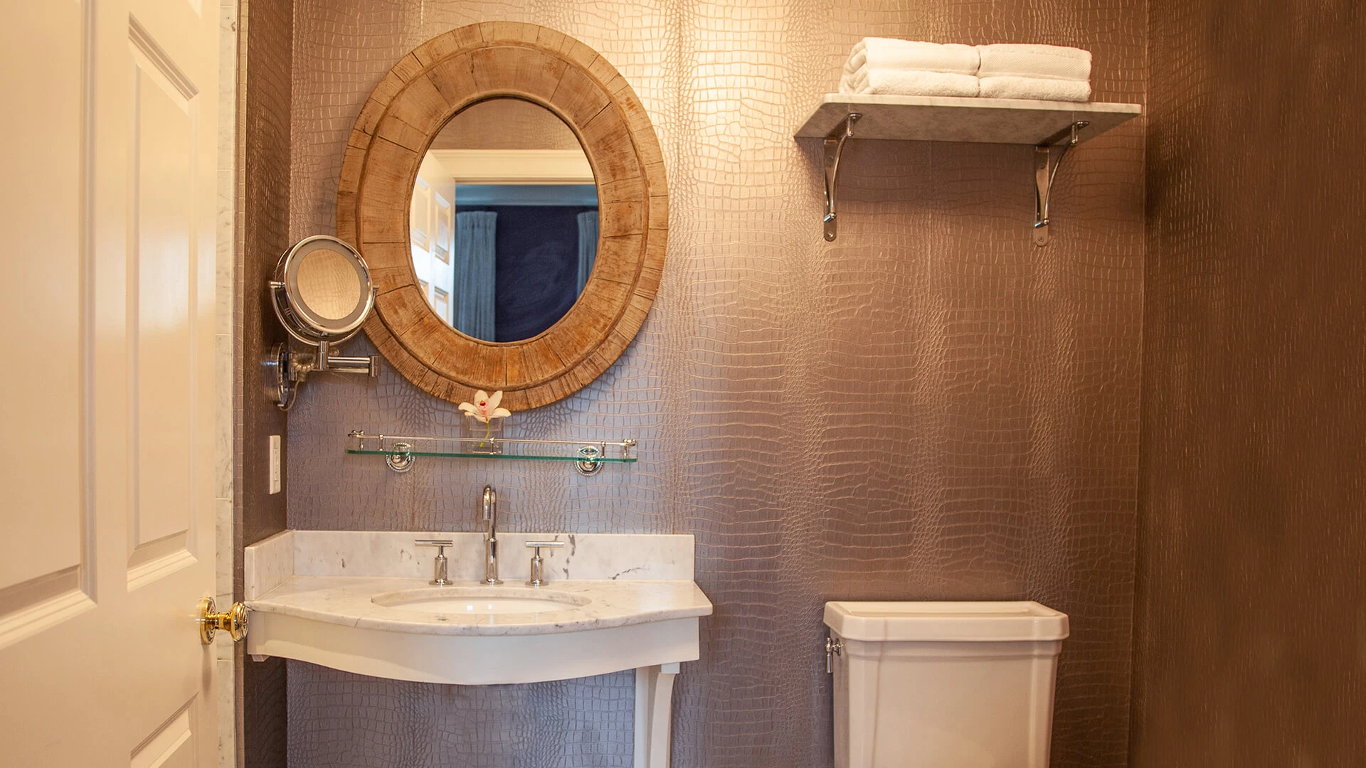 A bathroom with a marble sink, round mirror, and toilet