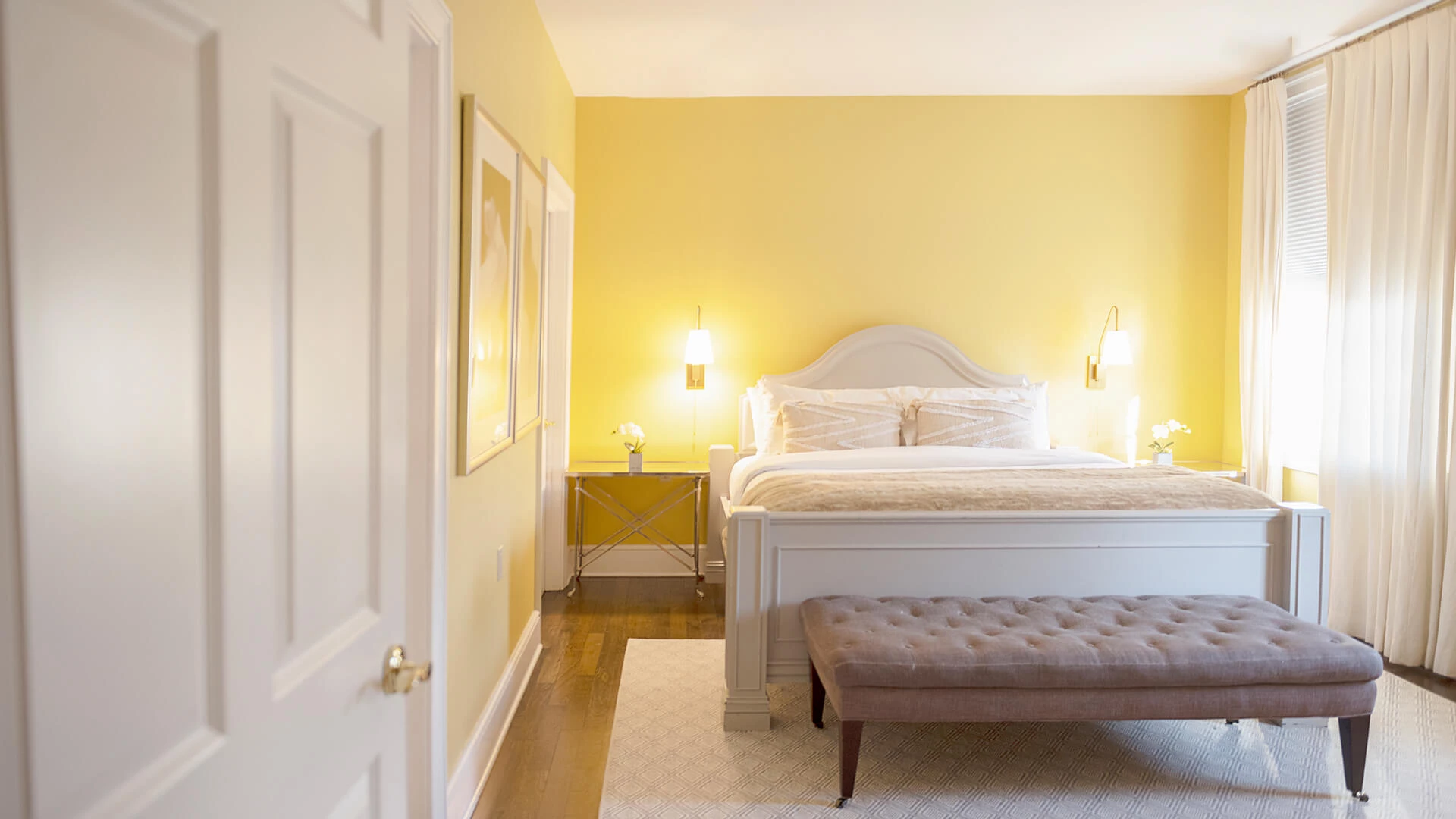 A wide view of a hotel room with a white bed, nightstand, and lamp.