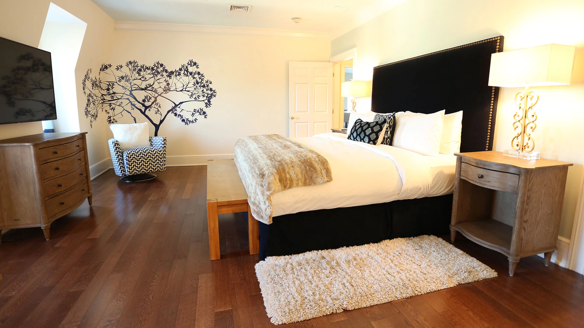 A wide view of a hotel room with a large bed, chair, TV, and rug.