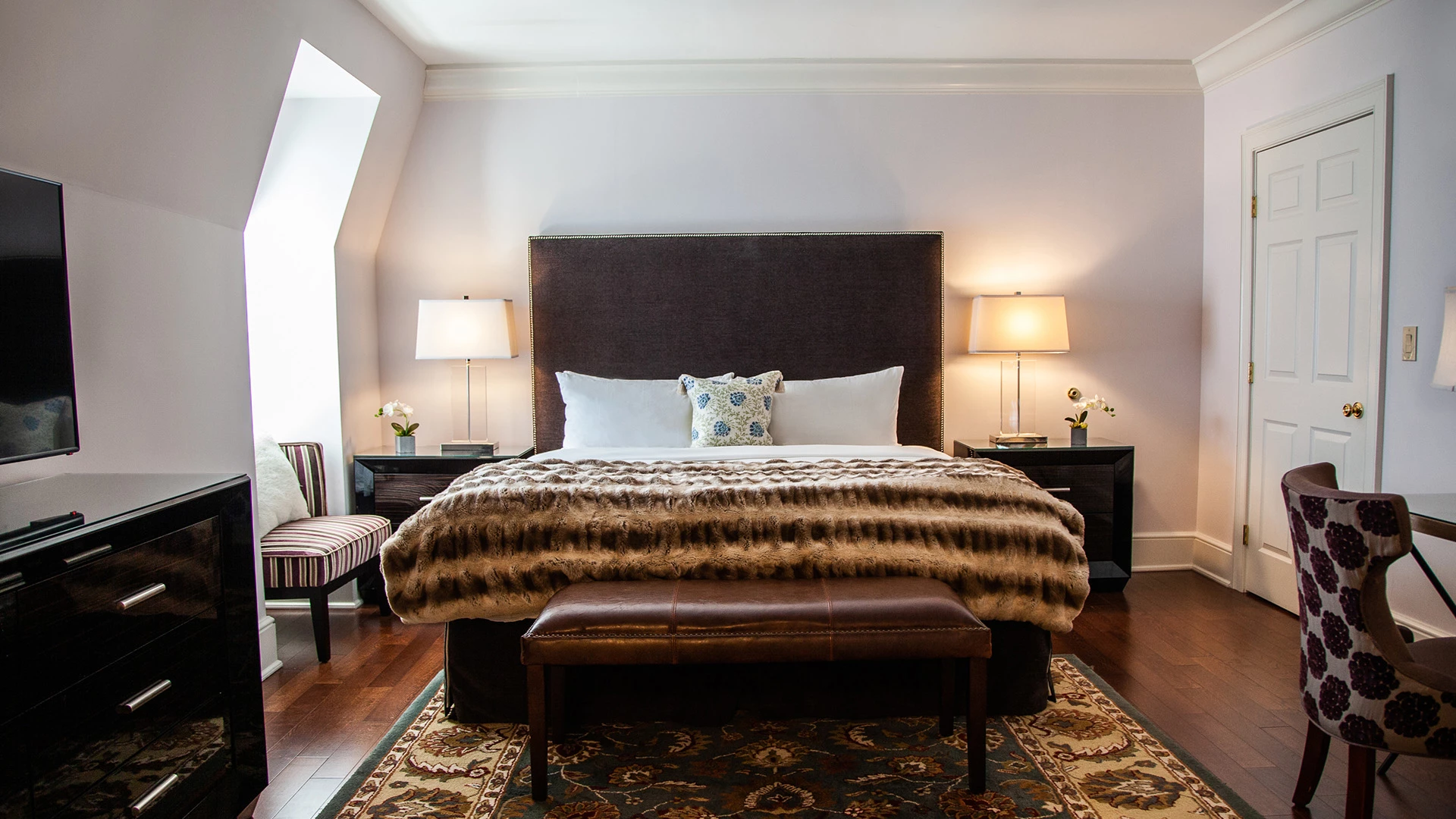 A hotel room with a large bed, two nightstands, a TV, and a chair