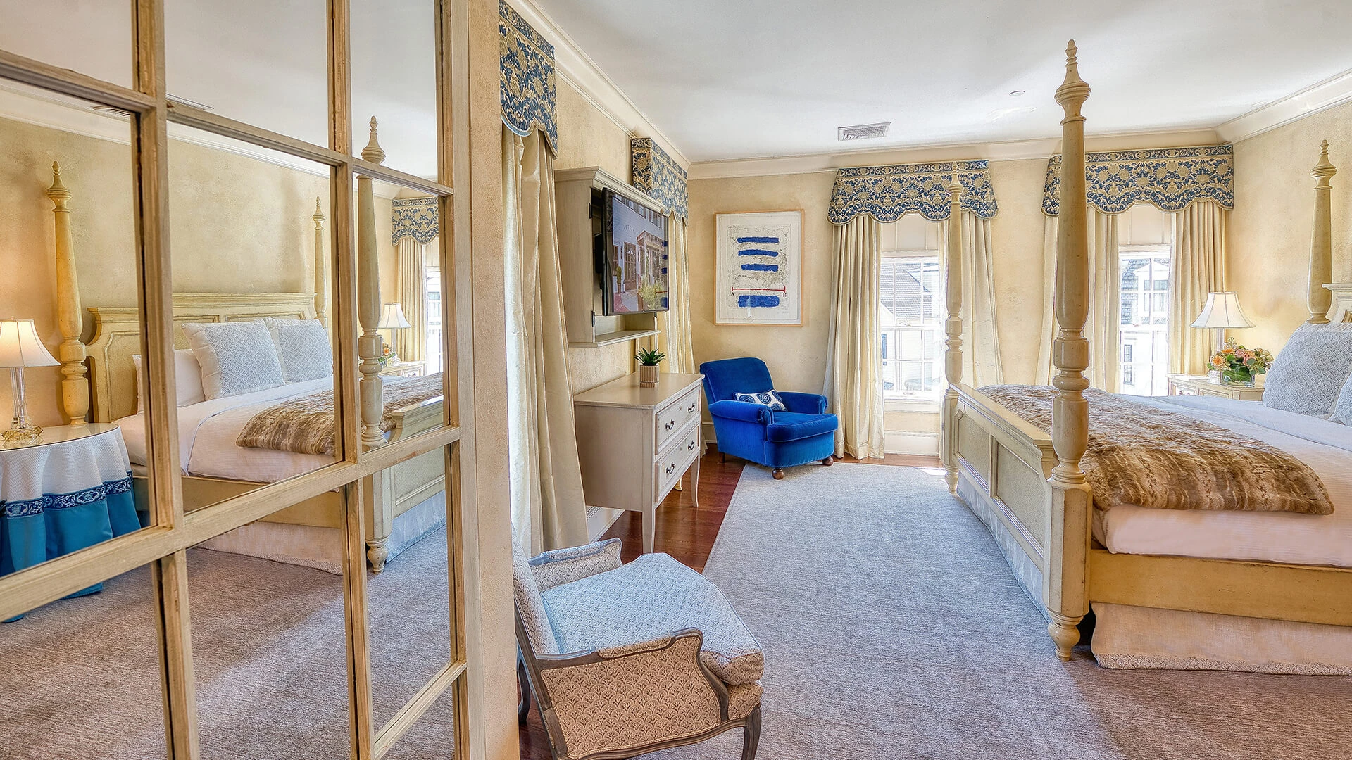 A wide view of a hotel room with a four-poster bed, mirrored wall, and sitting area.