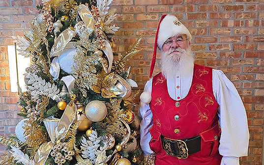 a man in a garment next to a christmas tree