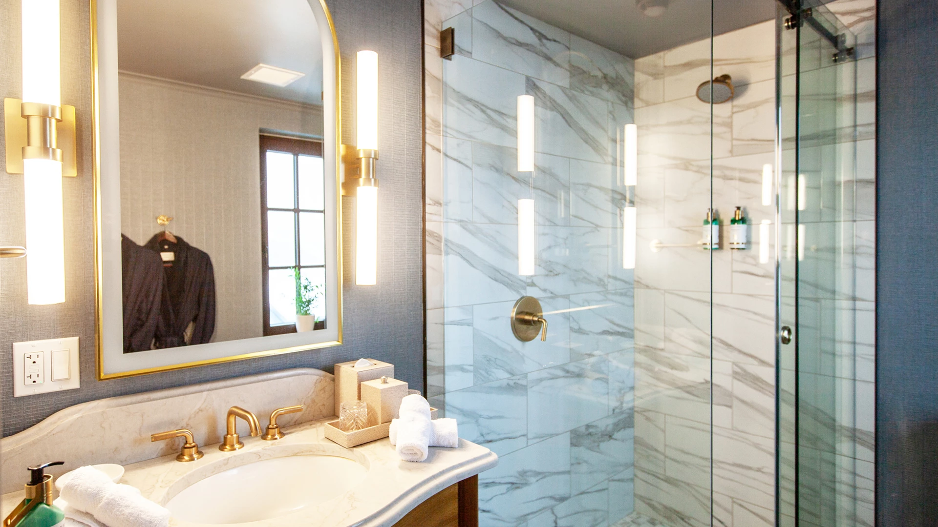 A bathroom with a marble shower, gold fixtures, and a glass enclosure