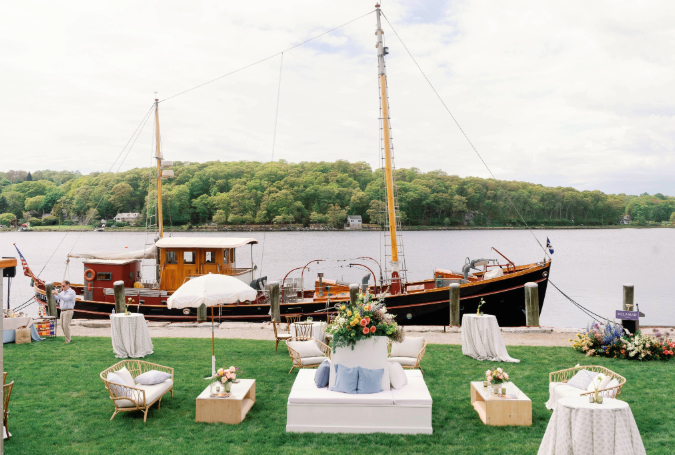 a group of chairs and tables on grass next to a boat