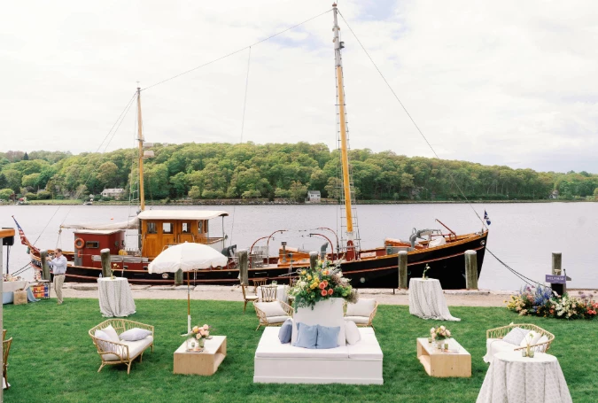 a group of chairs and tables on grass next to a boat