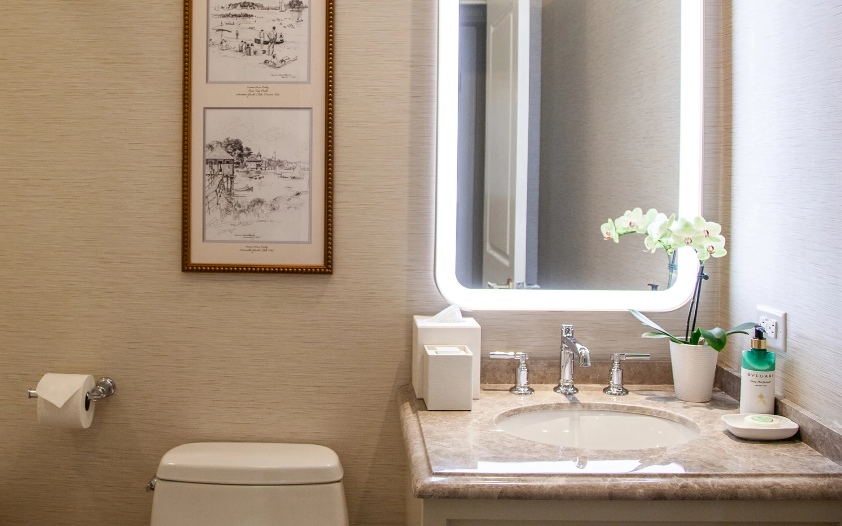 A clean bathroom with a marble countertop, white sink, and toilet, accompanied by a framed picture on the wall.