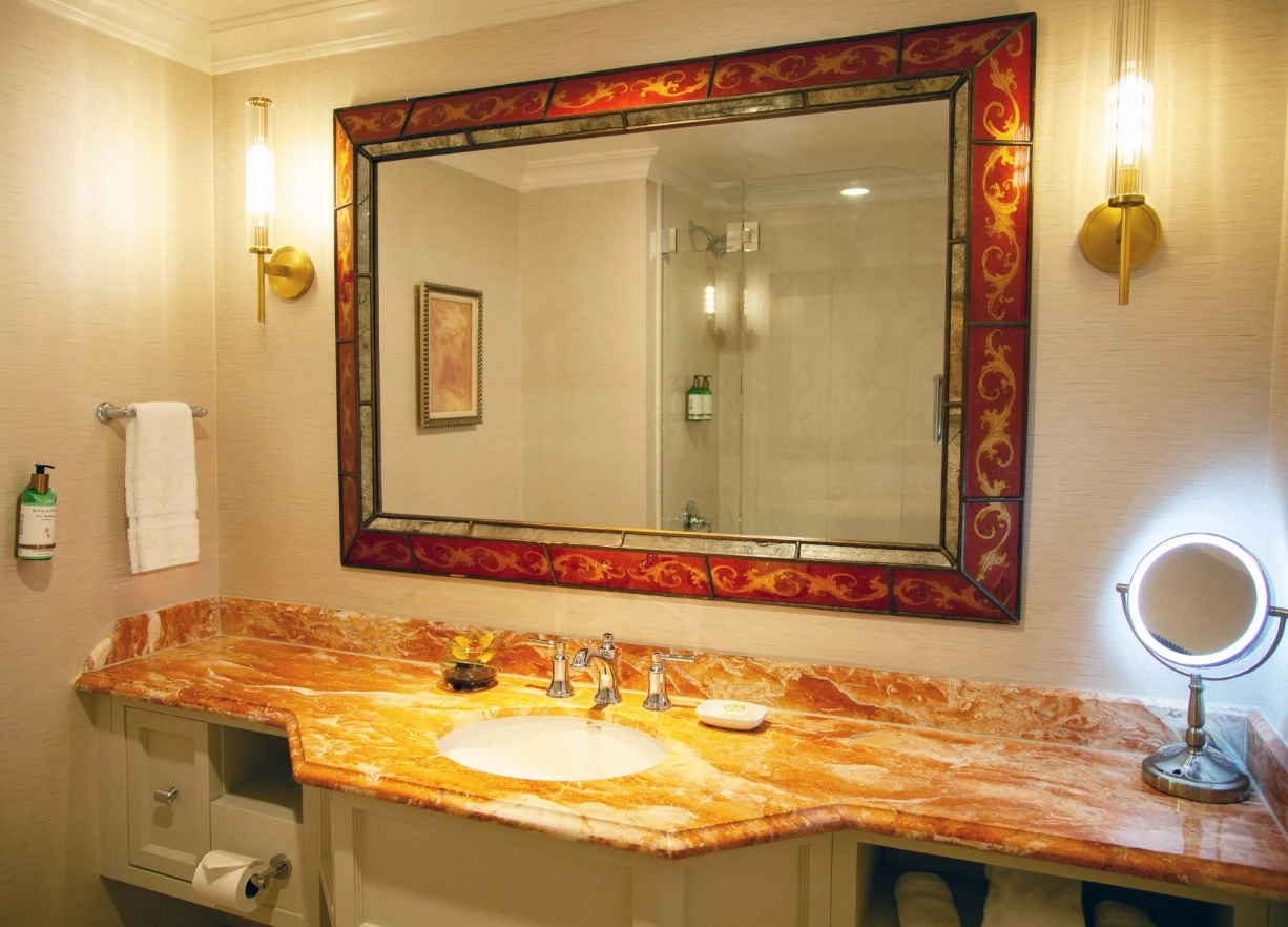 A bathroom vanity with a large ornate mirror, marble countertop, and wall sconces.