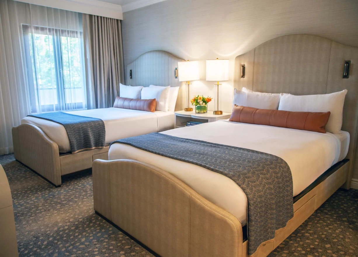 A hotel room with two beds, a window, and a nightstand.