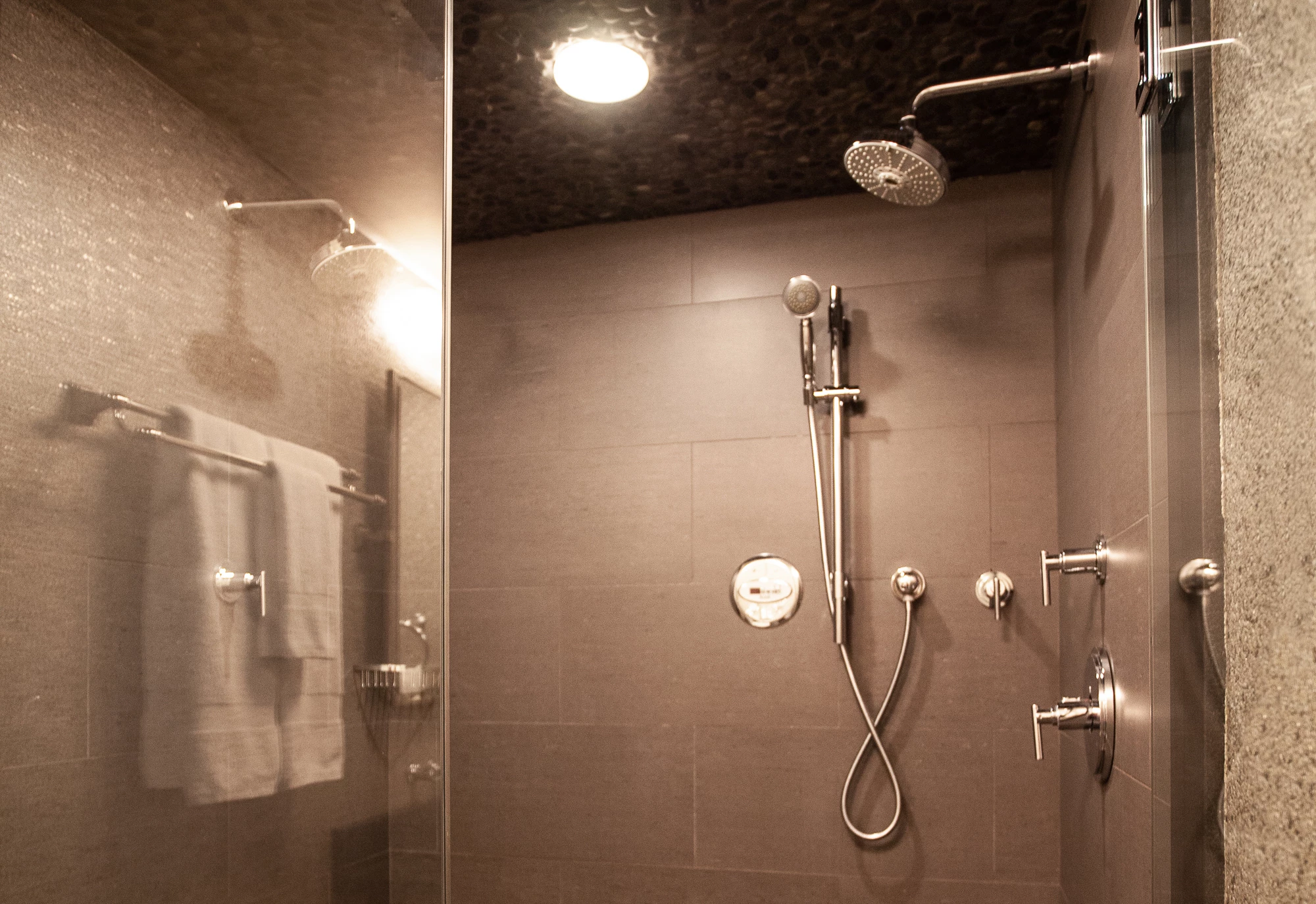 A modern bathroom shower with tiled walls, a rain showerhead, body sprays, and towels.