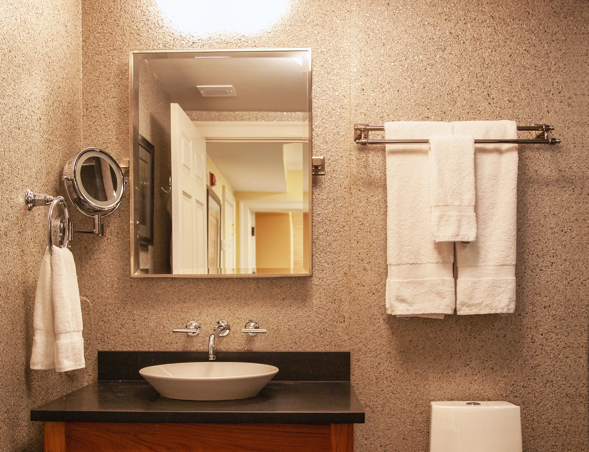 A bathroom with a sink, mirror, towels, and toilet.
