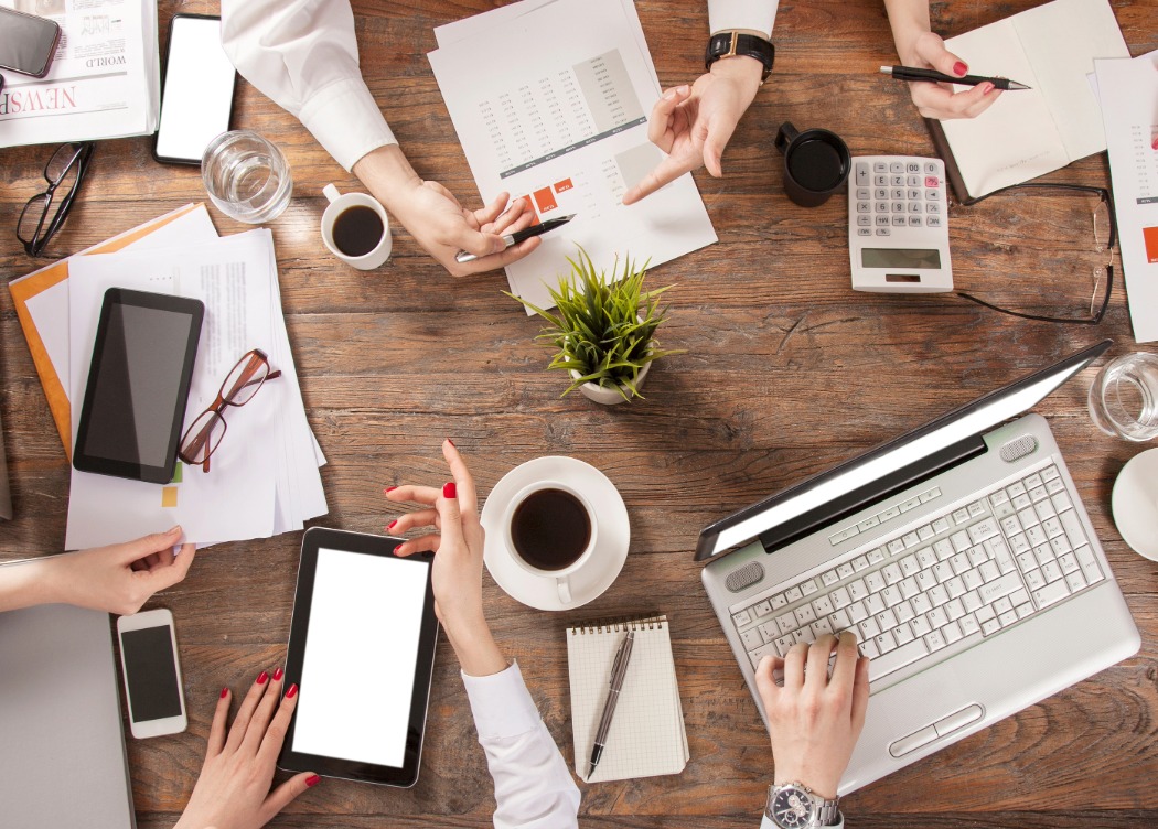 a group of people sitting around a table with laptops and tablets