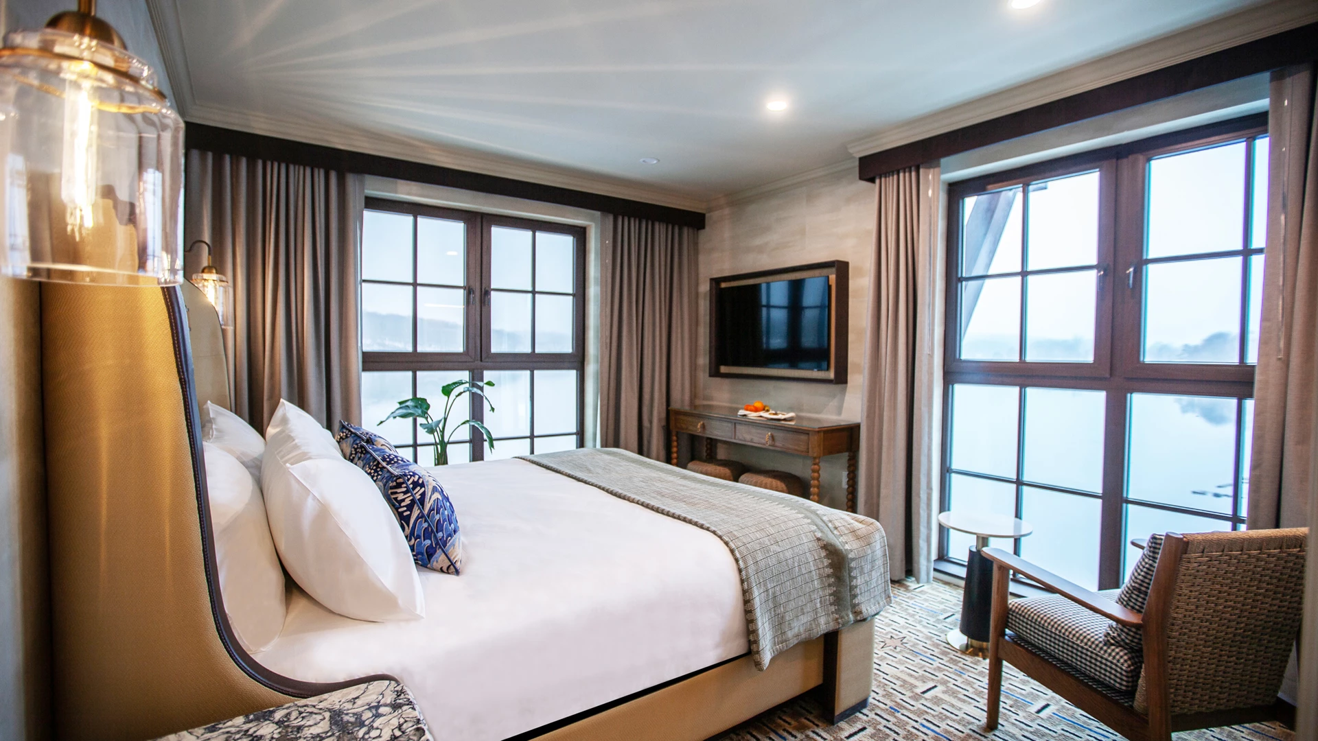 A hotel room with a bed, window, TV, chair, and lamp.