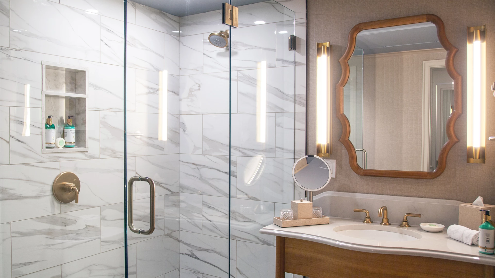 A modern bathroom with a glass-enclosed shower, marble tiles, and gold fixtures.