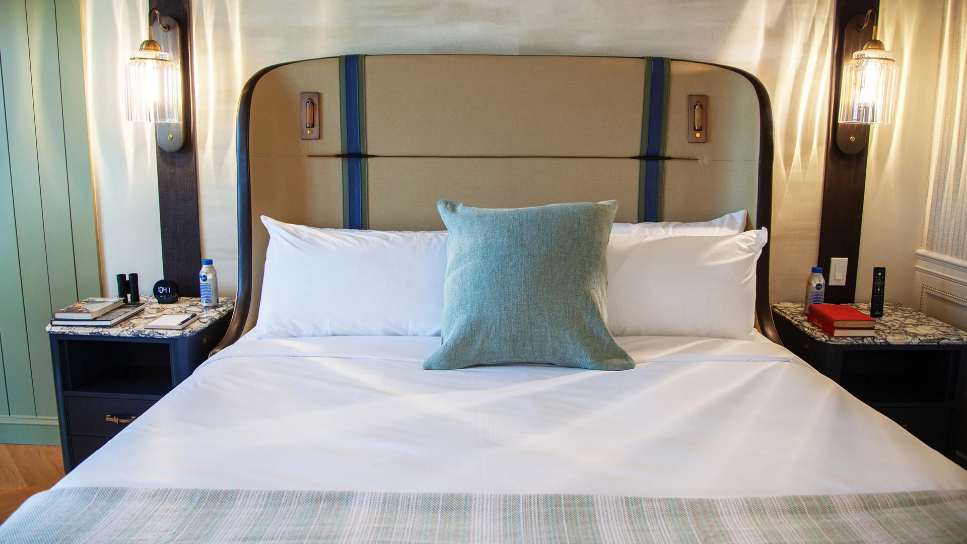A neatly made bed with white linens and a blue accent pillow