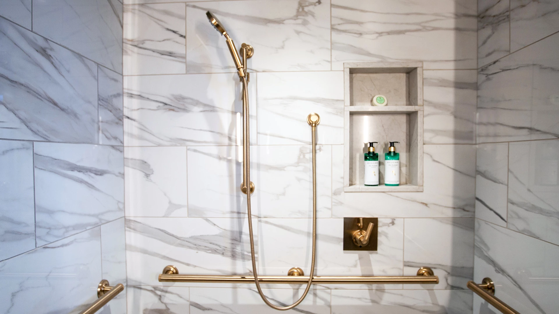 A shower with marble tiles and gold fixtures
