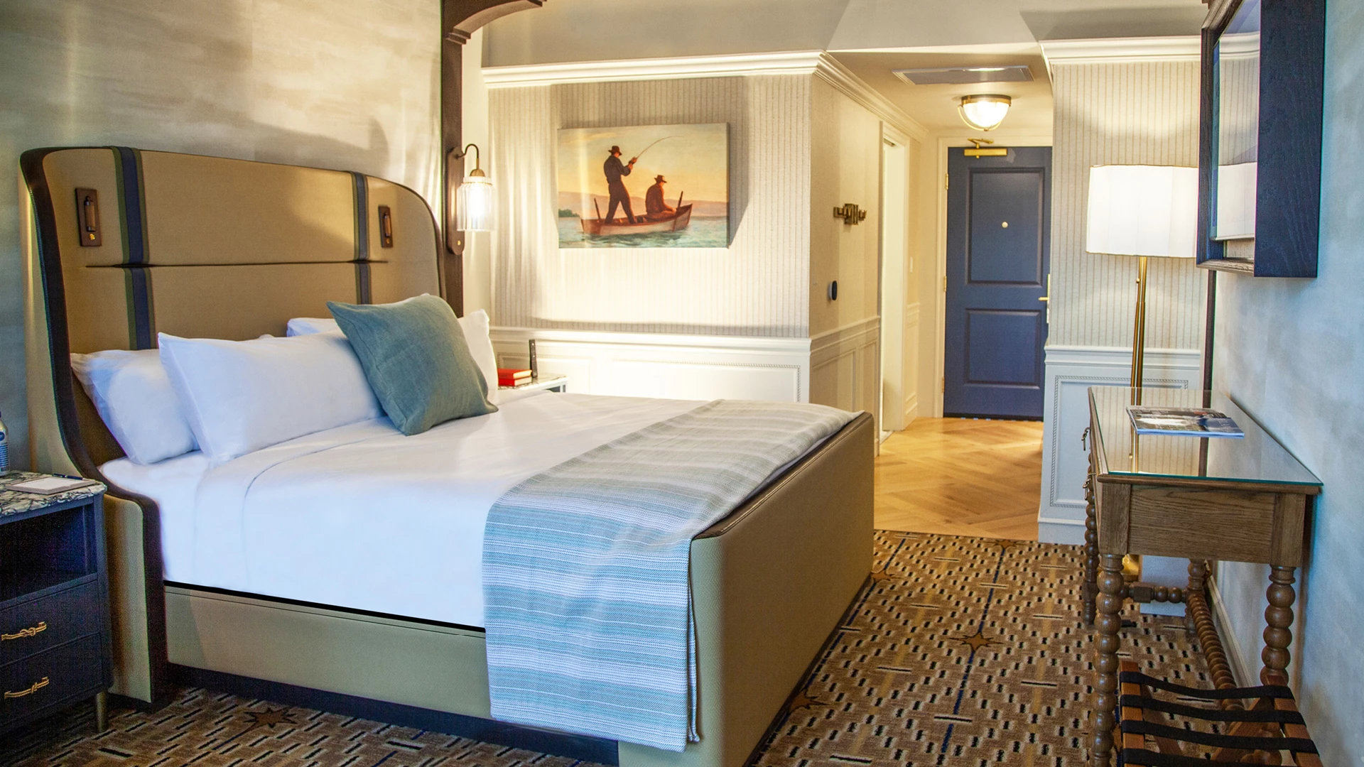 A hotel room with a bed, nightstand, desk, and lamp.