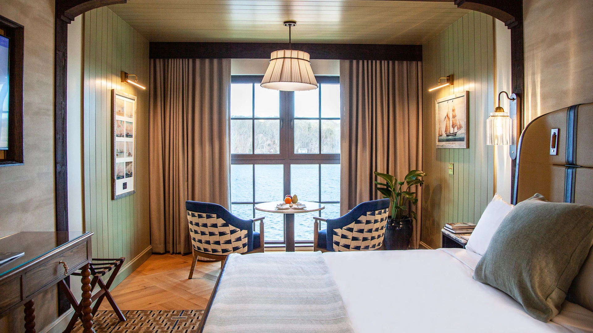 A hotel room with a large window, a seating area, and a bed.