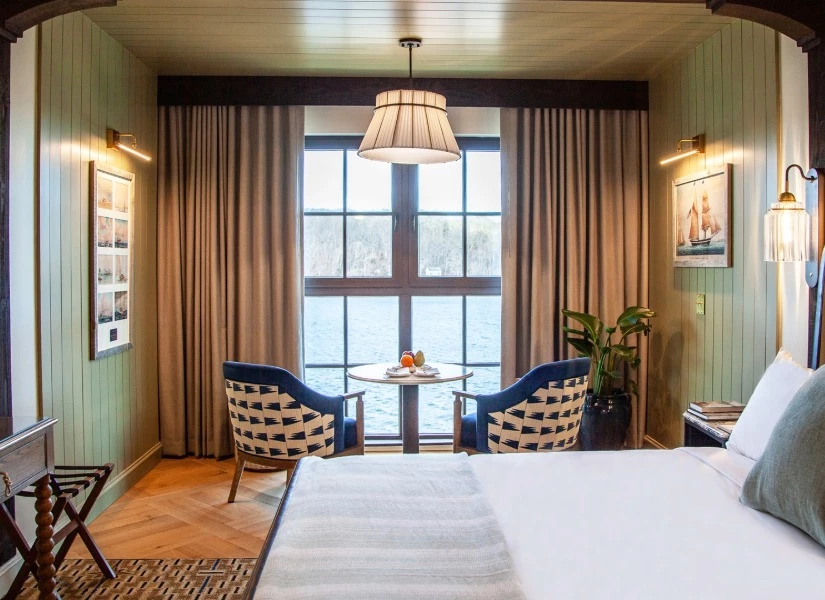A wide view of a hotel room with a bed, two chairs, a table, and a window with a view.
