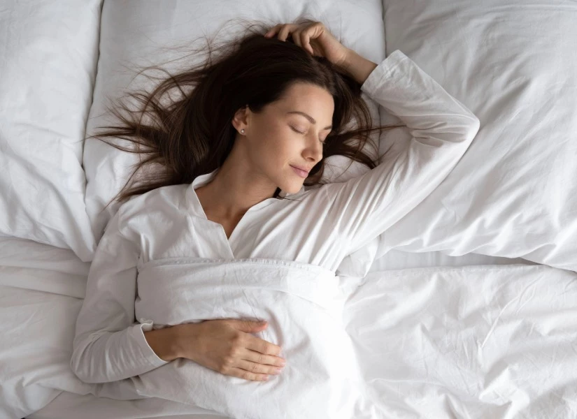 A woman lies on a bed with white bedding, sleeping or relaxing.