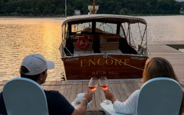 a couple of people sitting on a dock with wine glasses