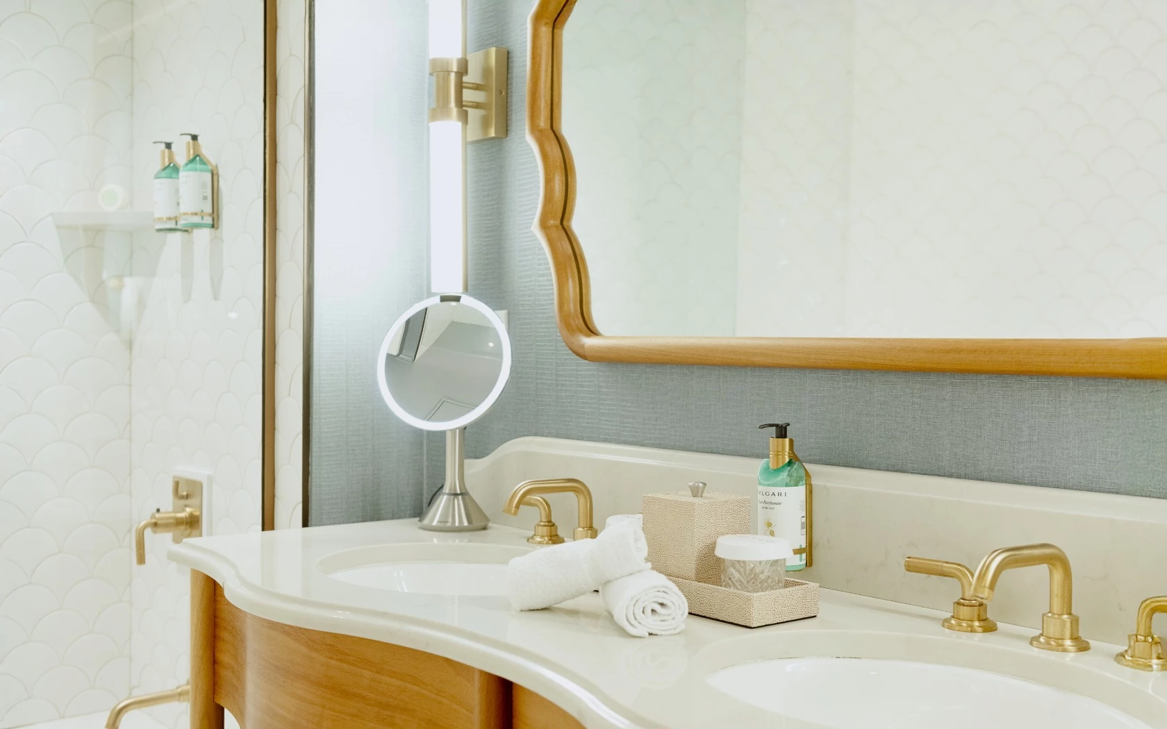 A clean and well-appointed bathroom sink area with double sink, gold faucets, and a large mirror.