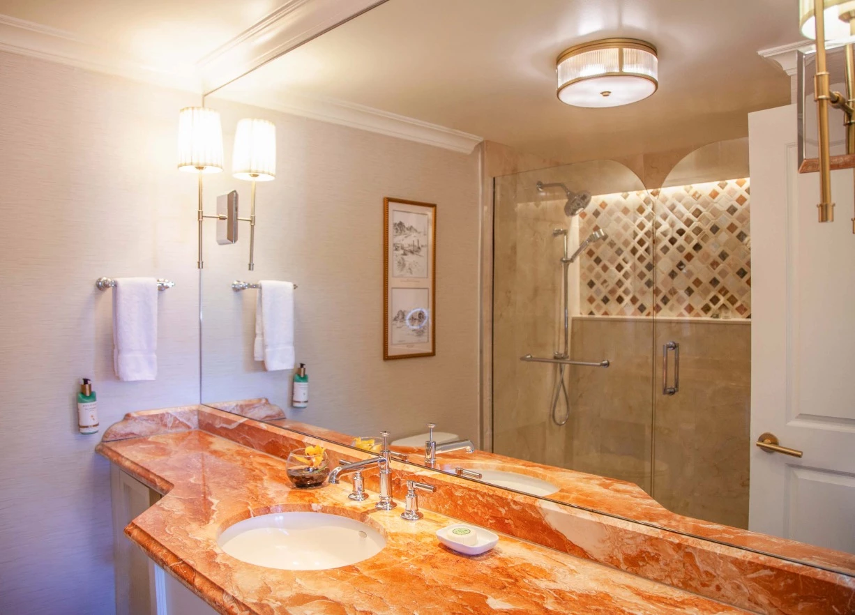 A bathroom with a marble countertop, double sink, and shower