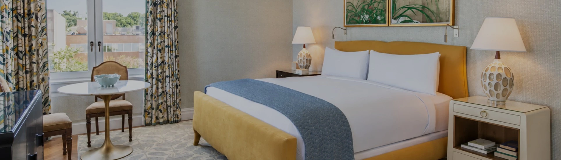 A hotel room with a bed, nightstand, lamp, table, and chair.