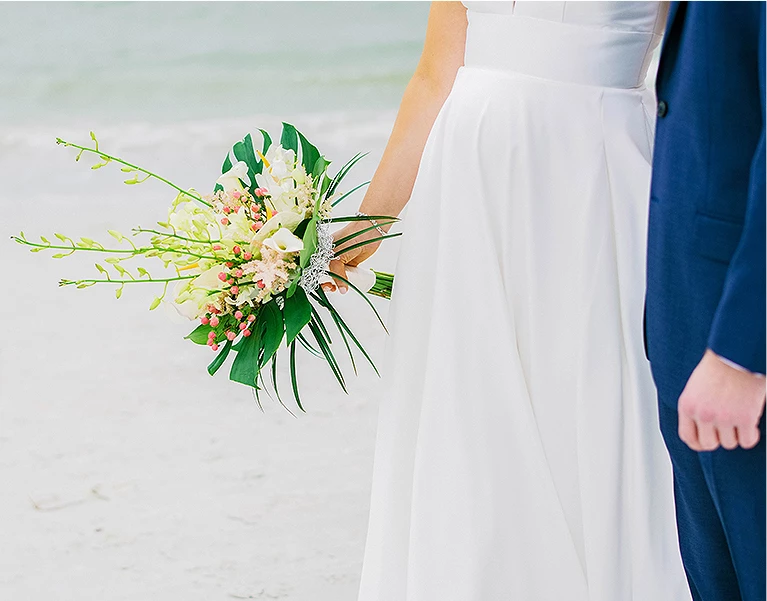 half of the body of bride and groom at the beach while she is holding her bridal boutique of roses