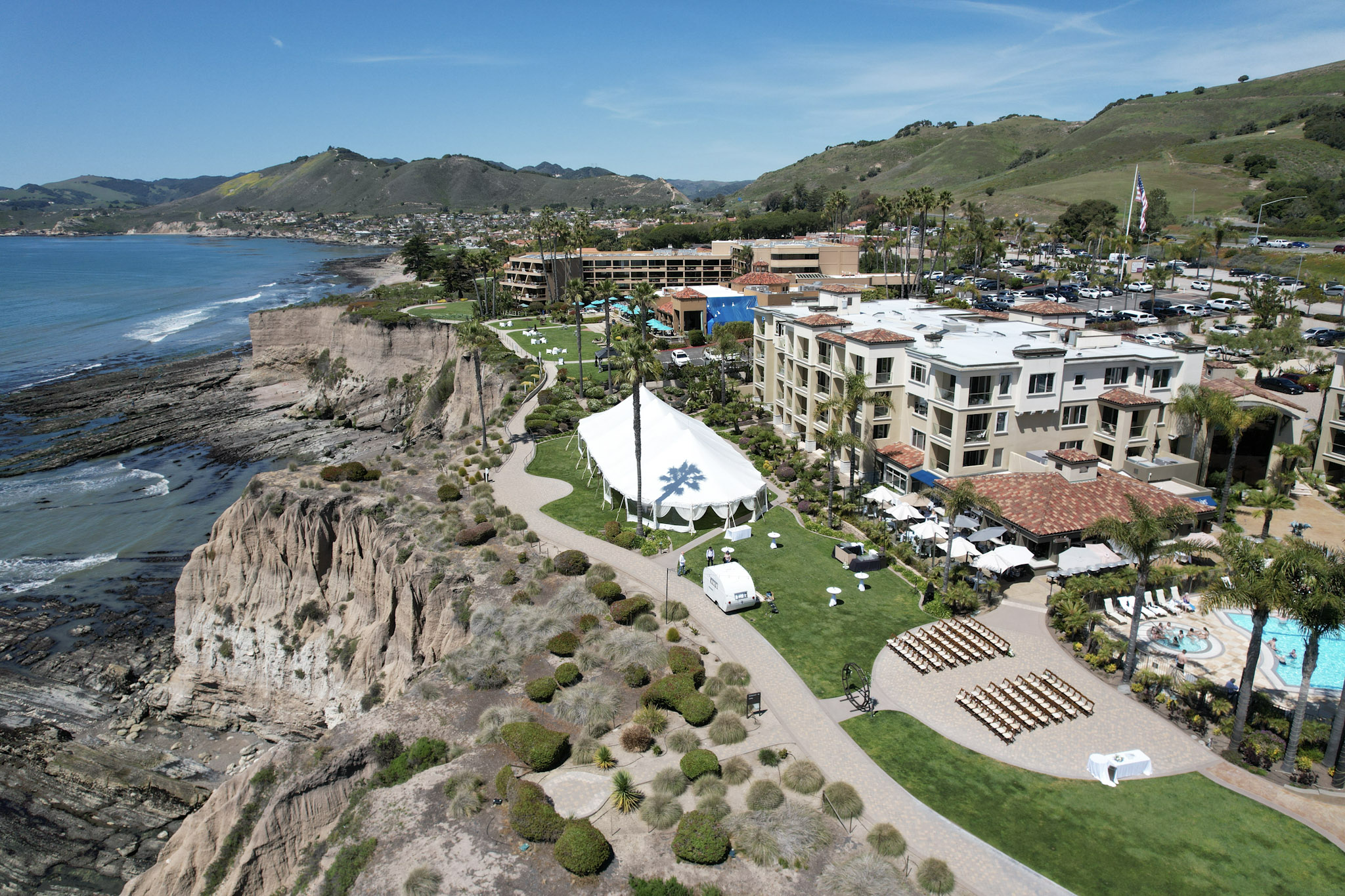 Aerial view of oceanfront wedding reception and ceremony setup at Dolphin Bay Resort & Spa in Pismo Beach — showcasing the cobblestone patio, coastal lawn, and tented celebration right beside the Pacific Ocean.