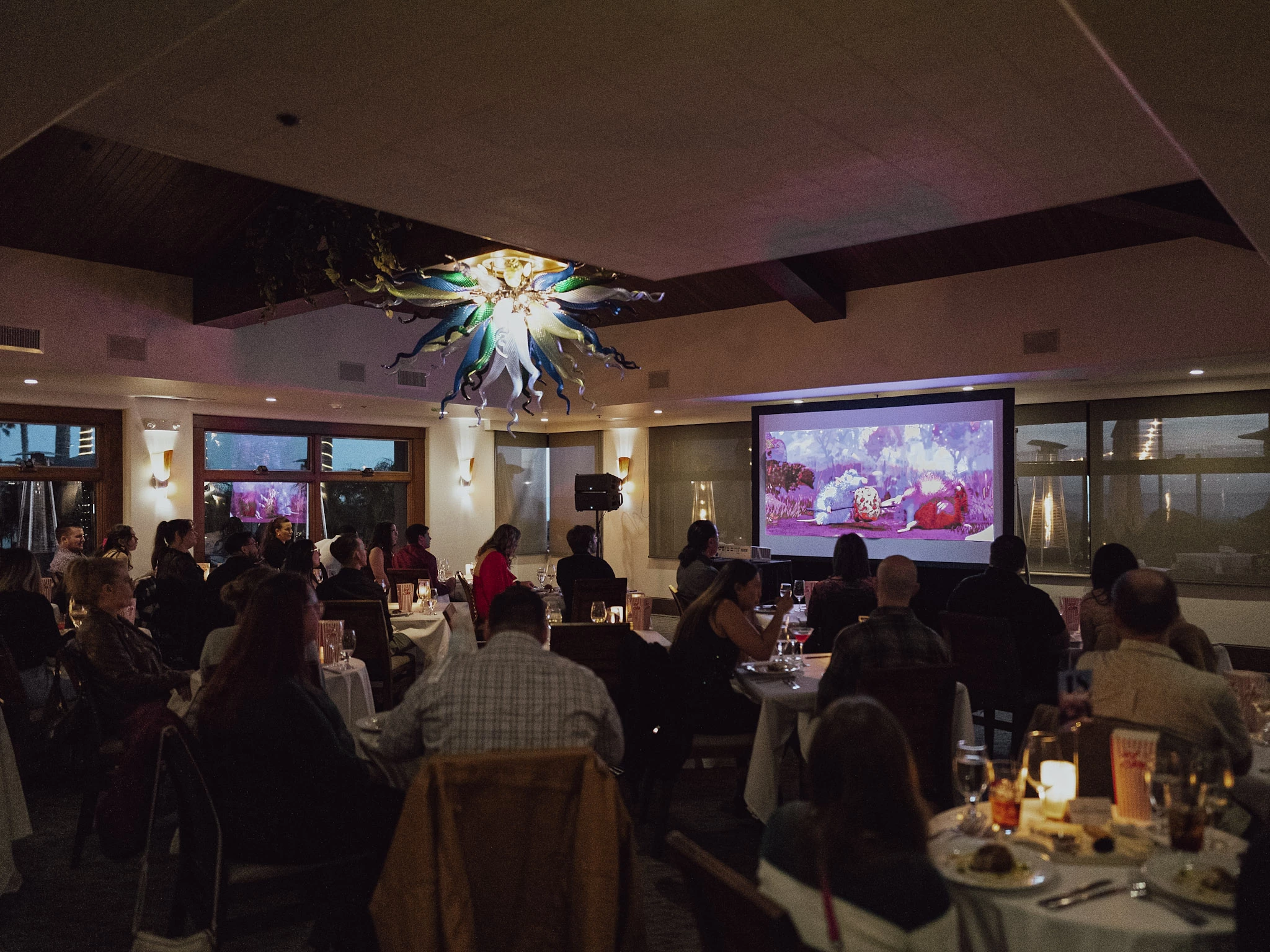 a group of people sitting at tables in a room with a large projector screen
