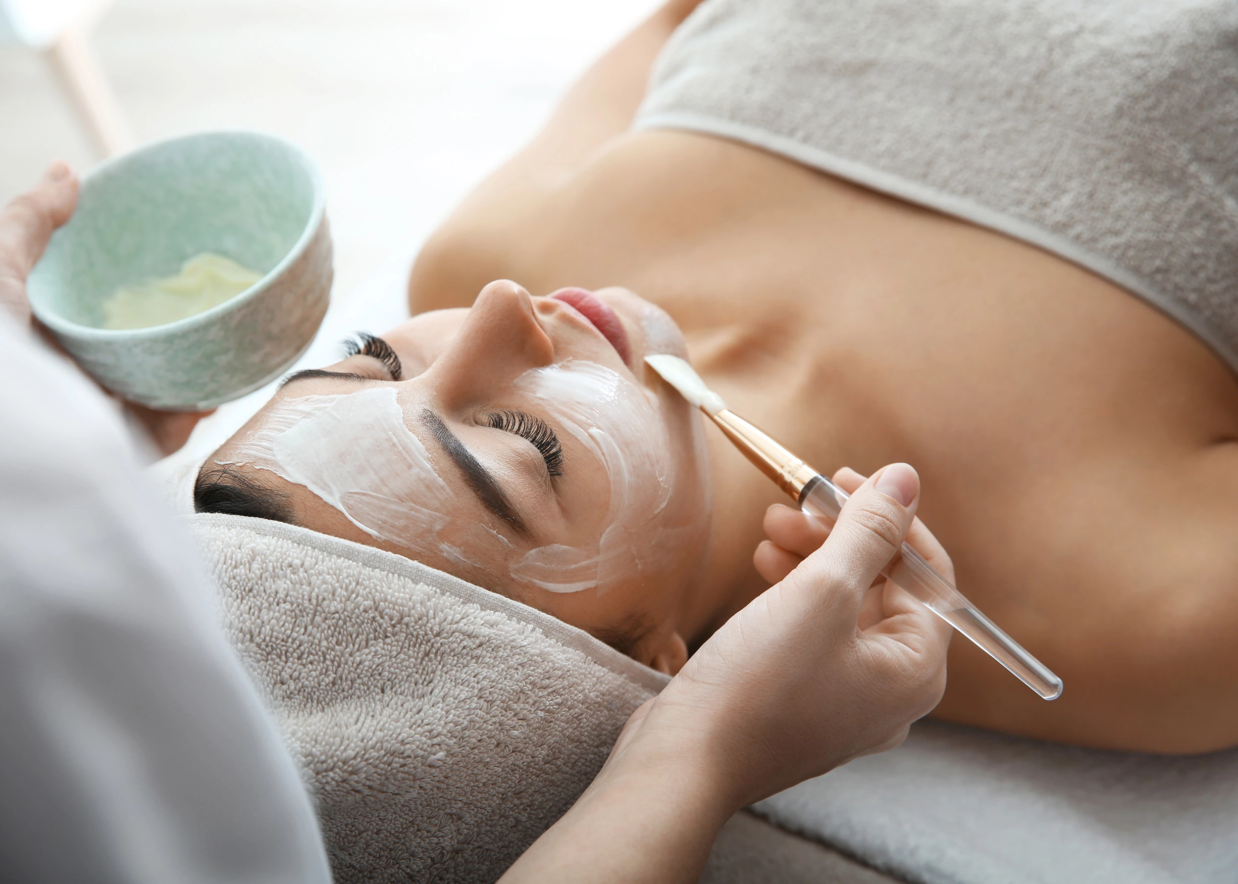 a woman lying down with a brush and a white mask on her face
