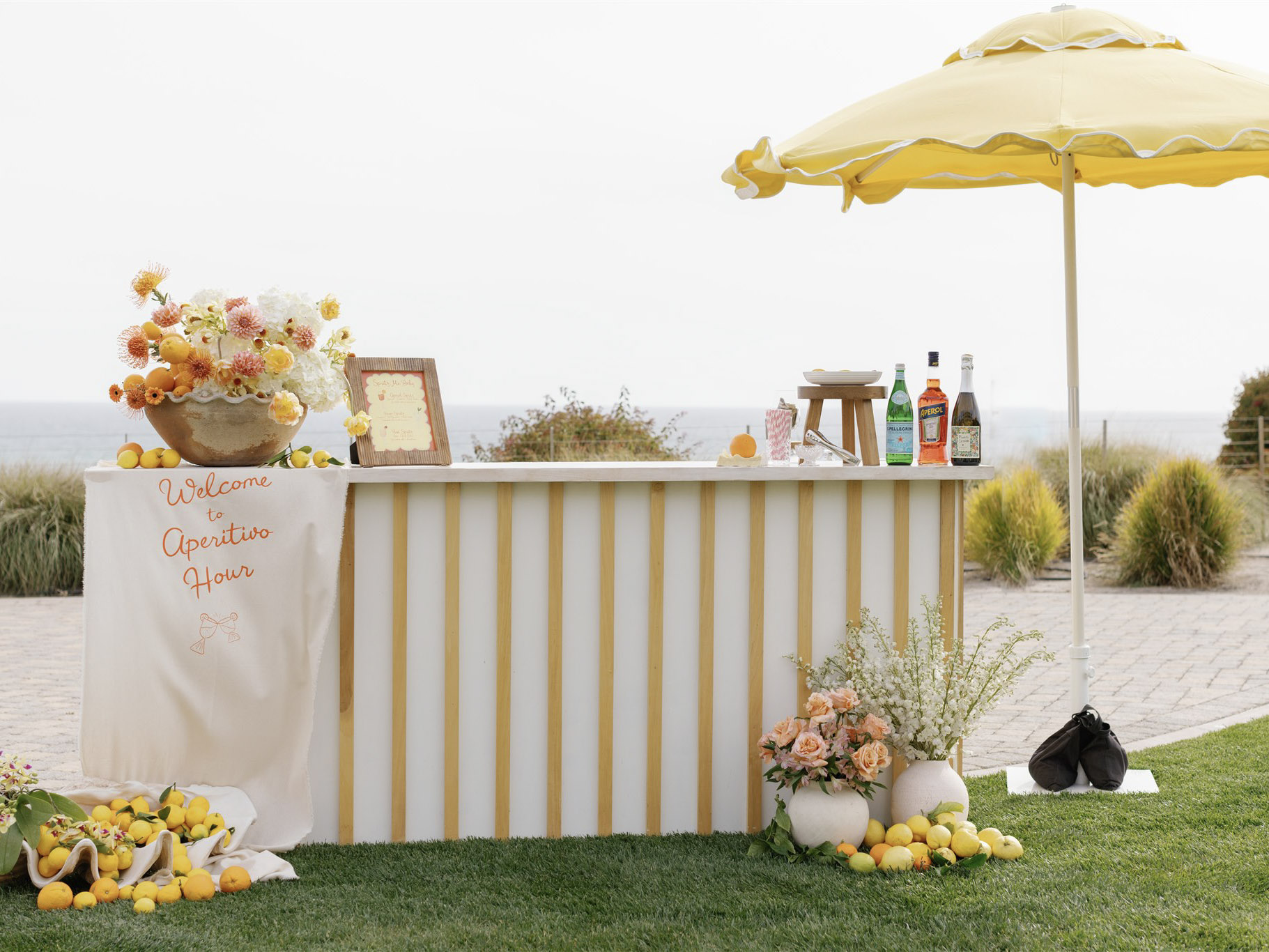 Italian coastal–inspired aperitivo bar setup with yellow stripes, lemons, and ocean views at Dolphin Bay Resort & Spa in Pismo Beach — the perfect start to your wedding celebration.