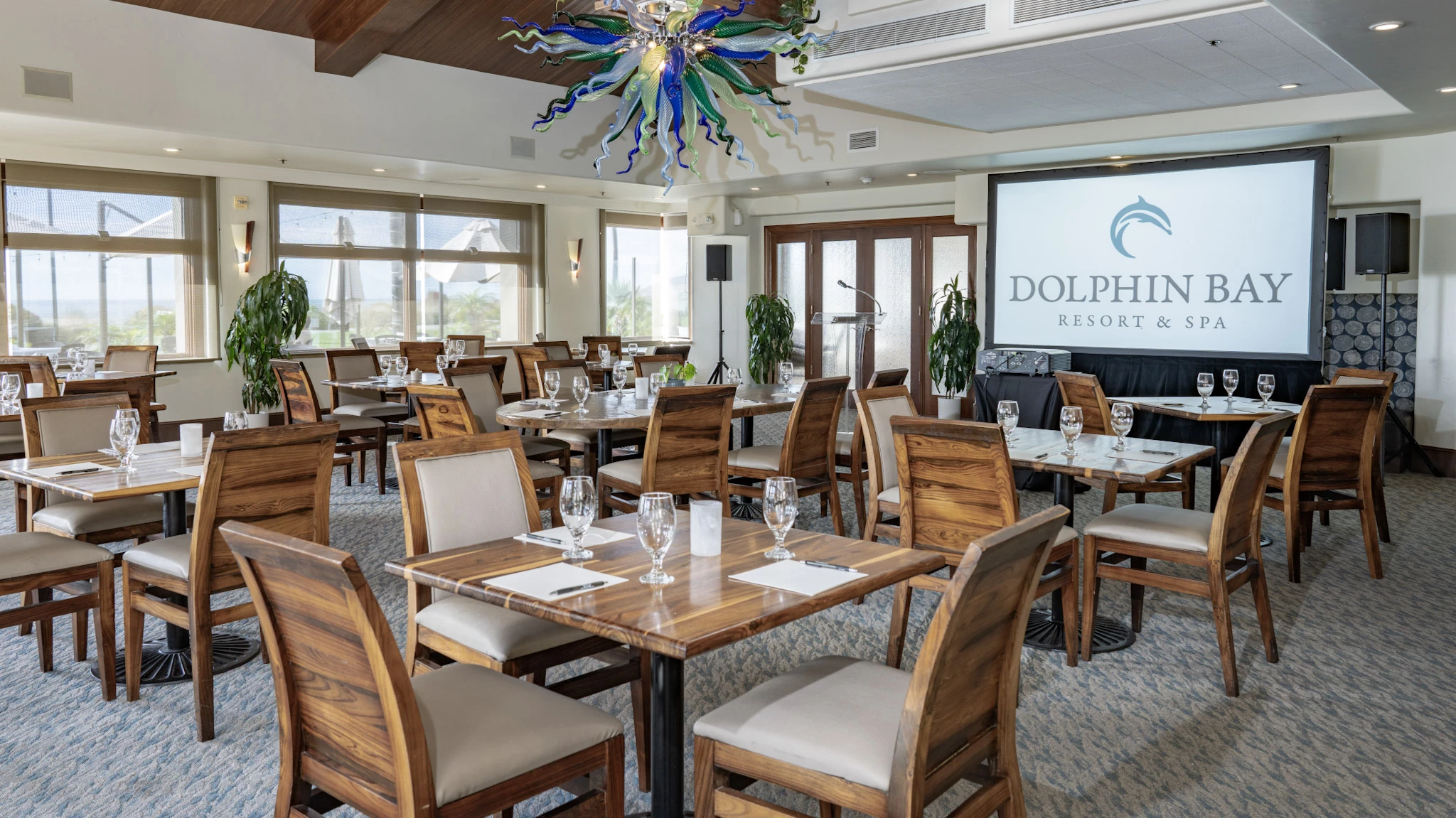Lido Dining Room & Lounge at Dolphin Bay Resort & Spa in Pismo Beach set in a banquet-style layout with separate tables facing a screen — perfect for workshops, retreats, and small conferences with partial ocean views.