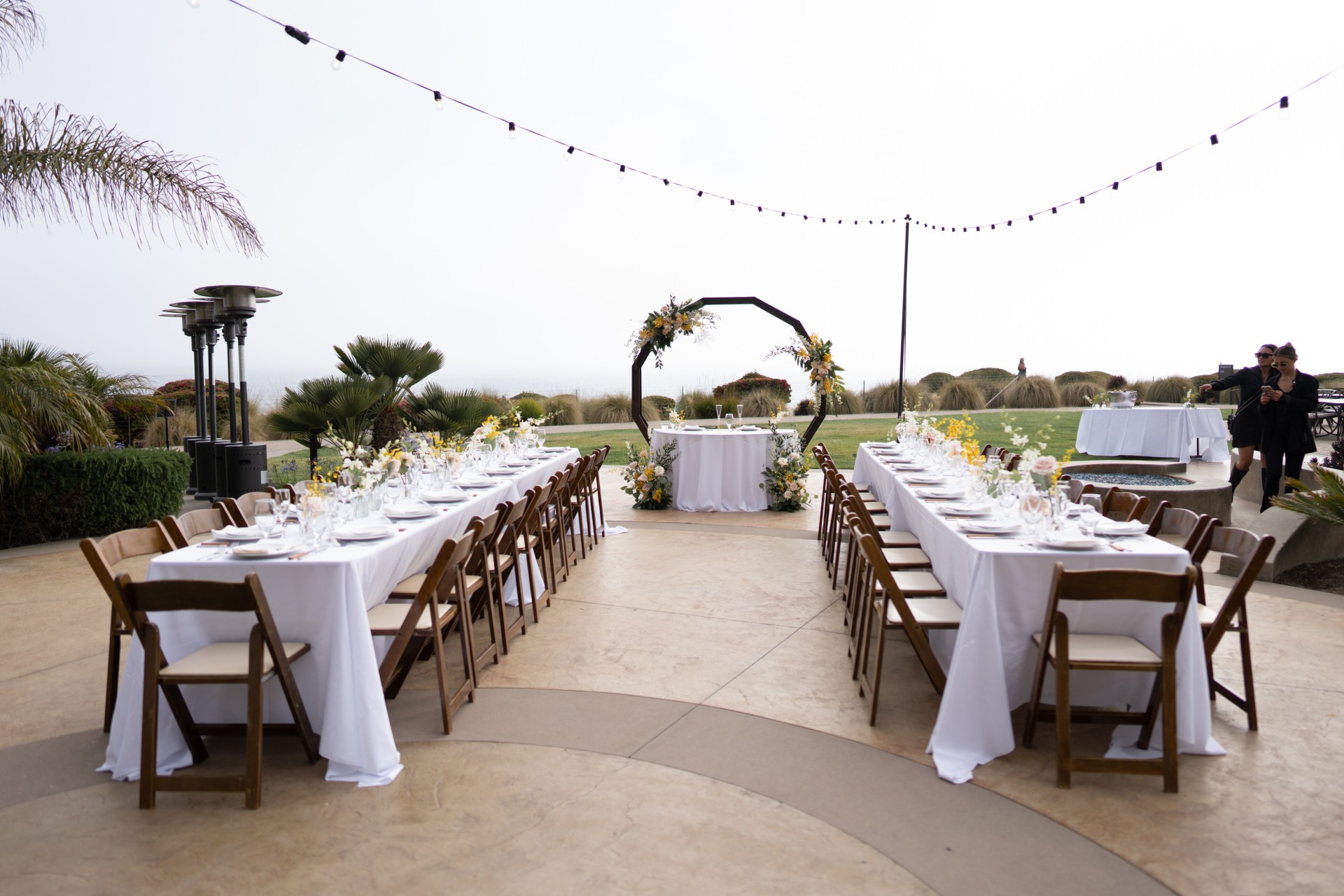 Fireside Patio at Dolphin Bay Resort & Spa in Pismo Beach — two long tables with a sweetheart table, ocean views, and outdoor heaters creating a warm, romantic setting for wedding receptions.