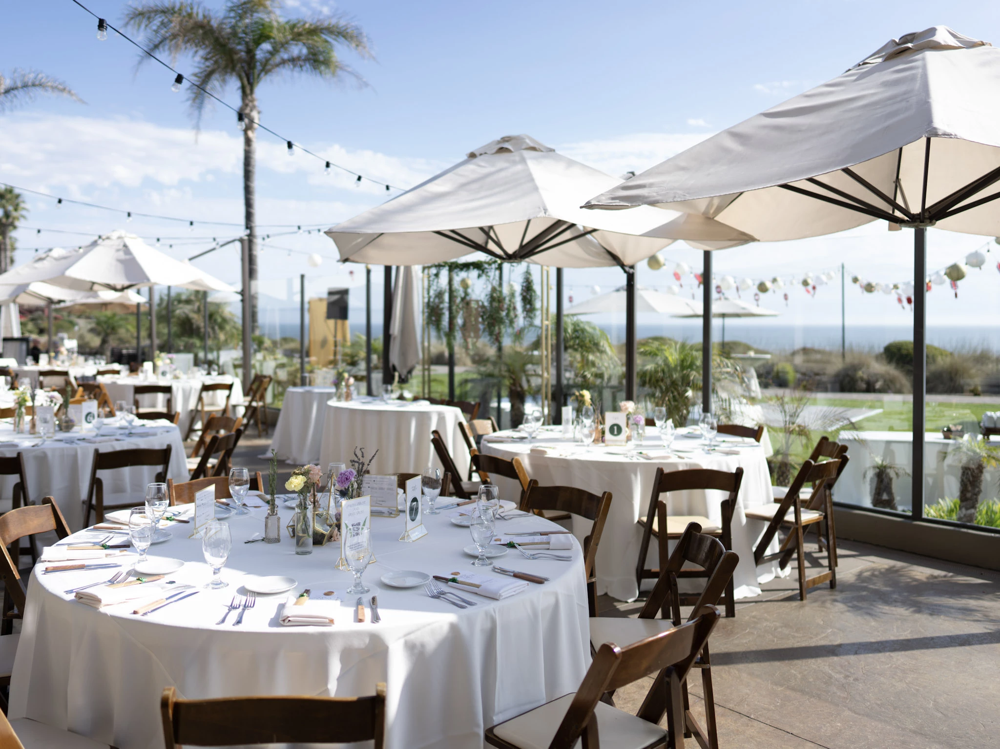 Luxury Pismo Beach customizable event space at Dolphin Bay Resort with ocean views, white linens, palm trees, and lantern-lit patio décor.