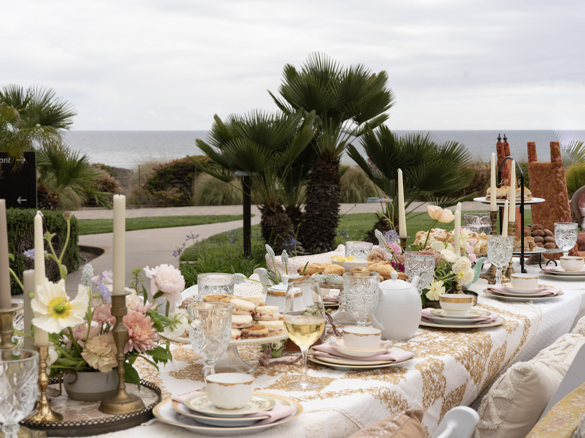 Oceanfront tea party on the fireside patio at Dolphin Bay Resort & Spa featuring a long floral table, fine china, and panoramic coastal views in Pismo Beach.