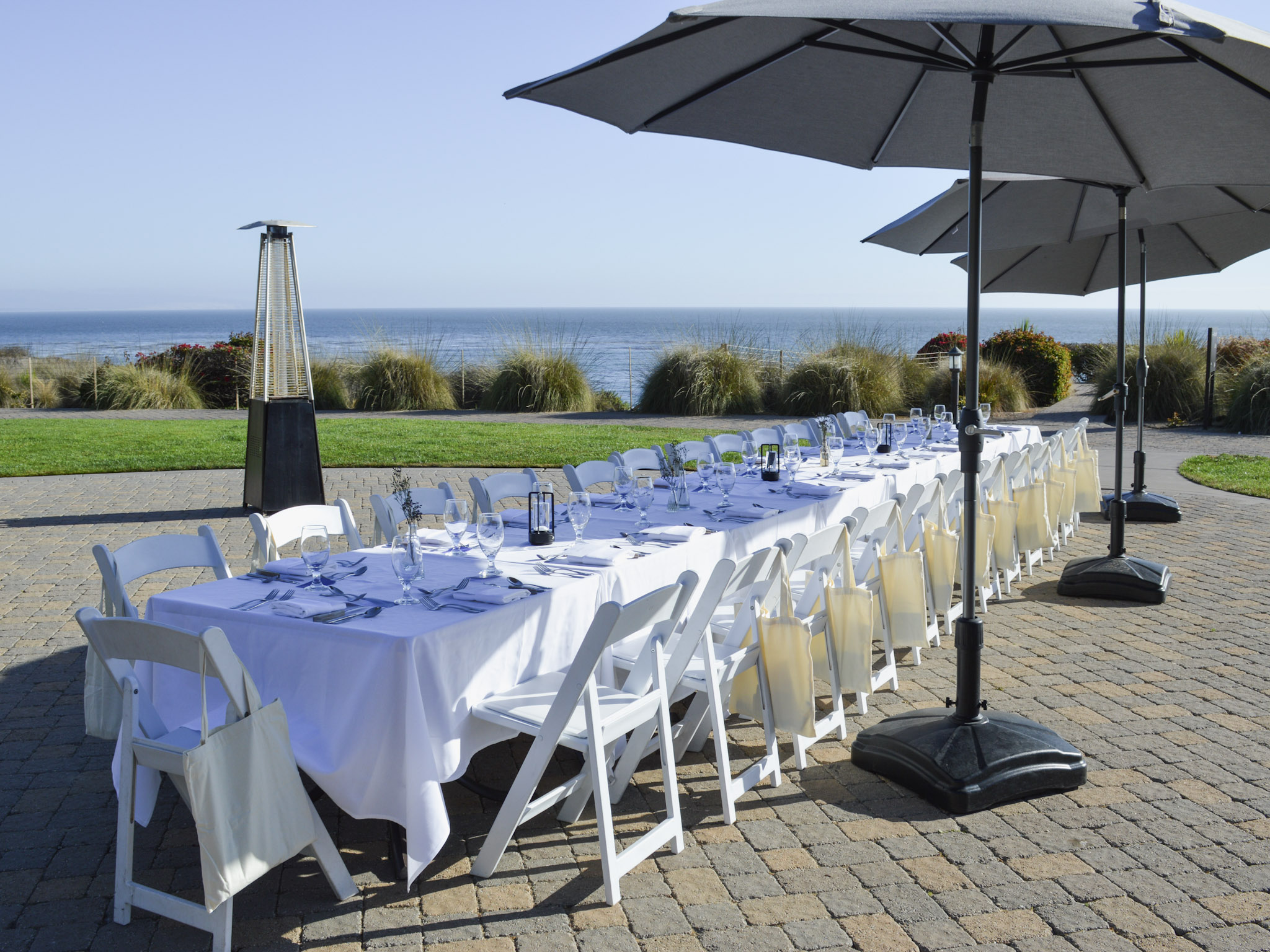 Elegant ocean-view birthday dinner on the cobblestone patio at Dolphin Bay Resort & Spa in Pismo Beach with white linens, umbrellas, and heaters overlooking the Pacific.