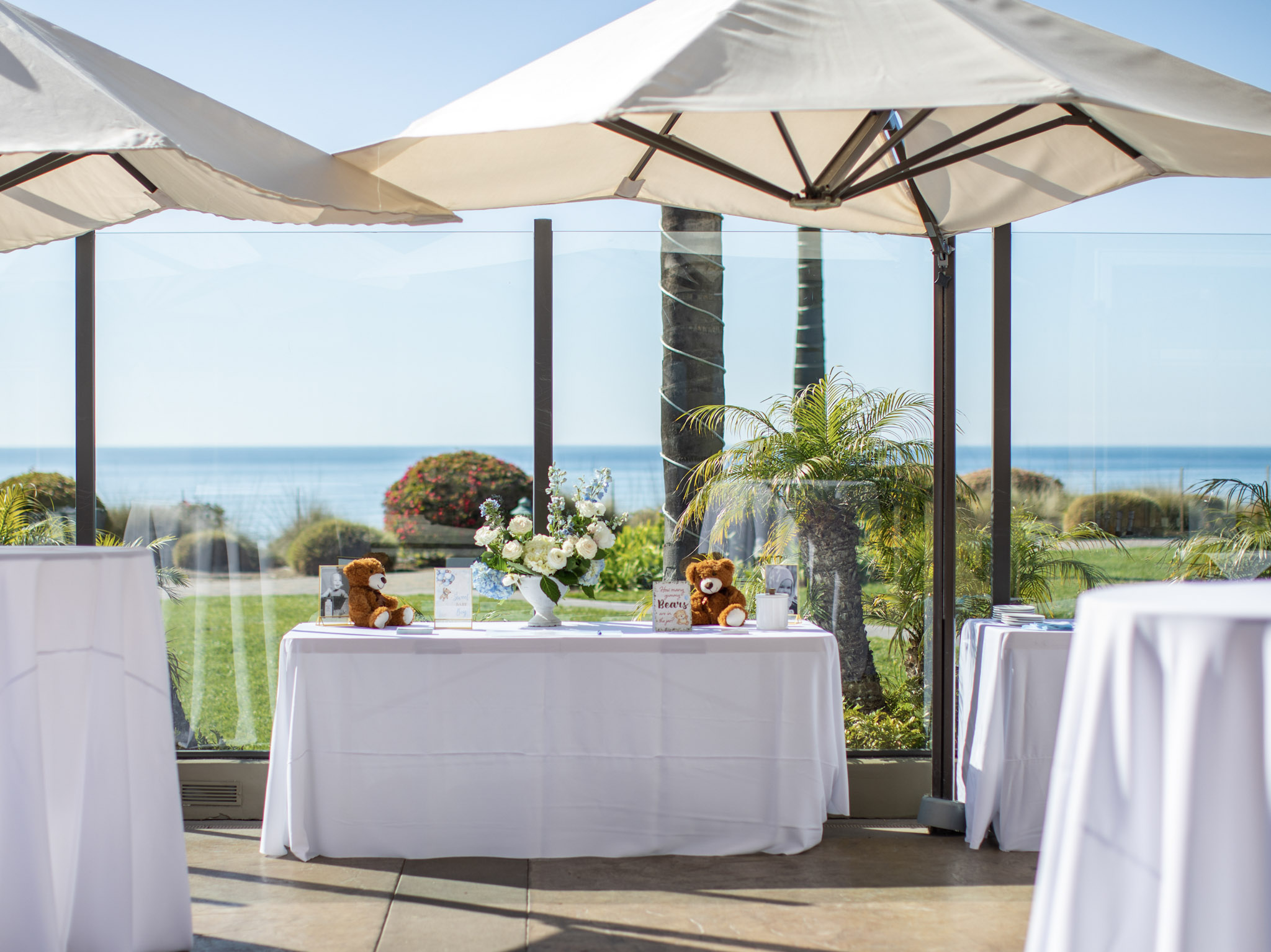 Oceanfront baby shower setup on the Lido Restaurant & Lounge patio at Dolphin Bay Resort & Spa in Pismo Beach featuring white linens, floral arrangements, and teddy-bear décor for a customizable celebration.