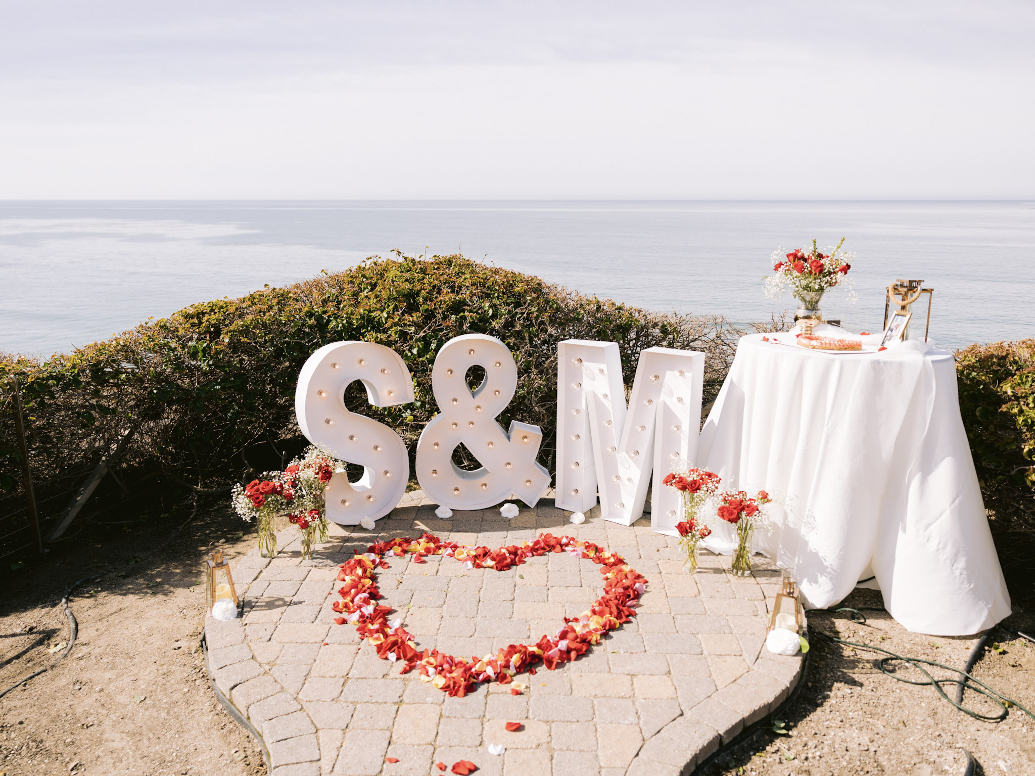 Romantic oceanfront proposal setup at The Point, Dolphin Bay Resort & Spa in Pismo Beach — featuring light-up “Marry Me” letters, rose petals, and a private dessert table overlooking the Pacific.