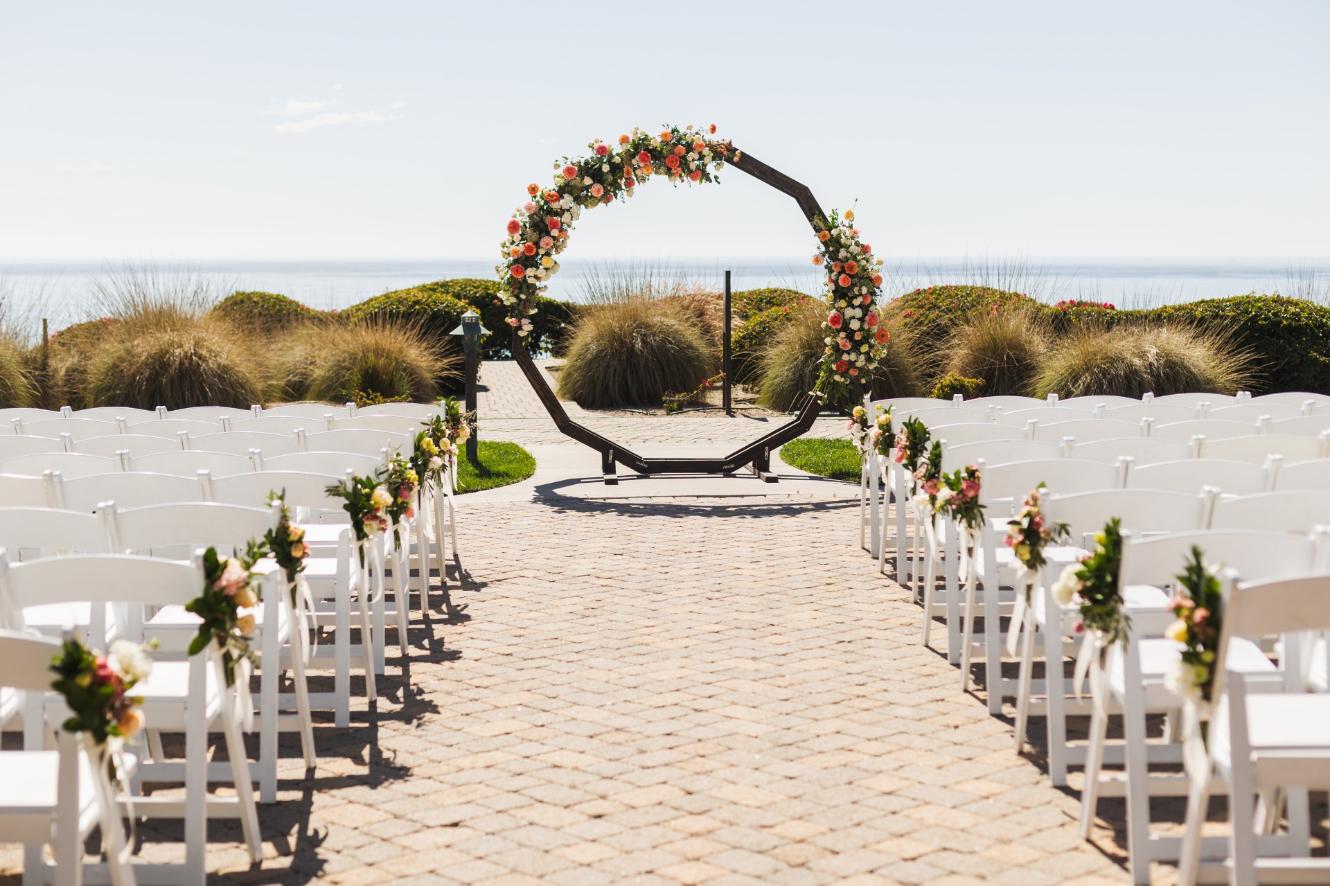 Oceanfront wedding ceremony on the cobblestone patio at Dolphin Bay Resort & Spa in Pismo Beach — elegant coastal setting with panoramic Pacific views and romantic cliffside ambiance.