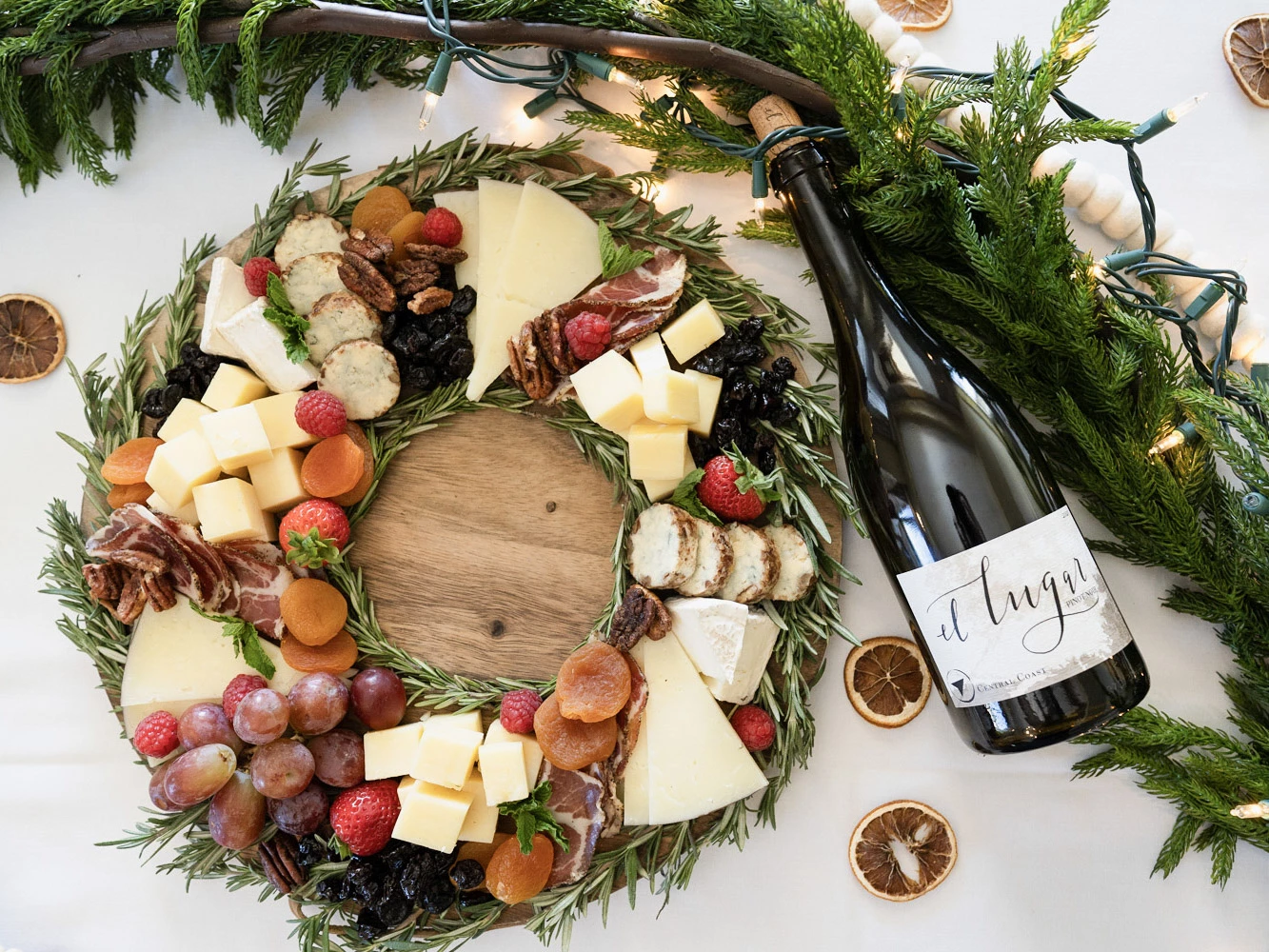 a cheese platter with fruit and nuts on a wooden board next to a bottle of wine