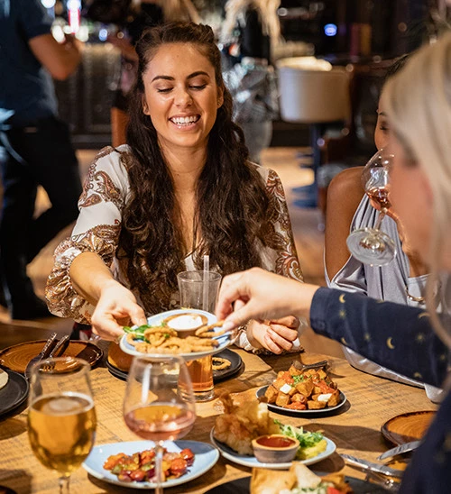 a woman smiling at a table with food and drinks
