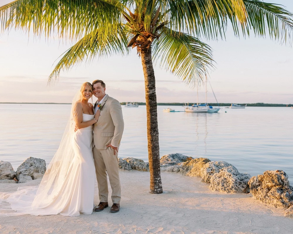 a man and woman in wedding attire standing on a beach with palm trees