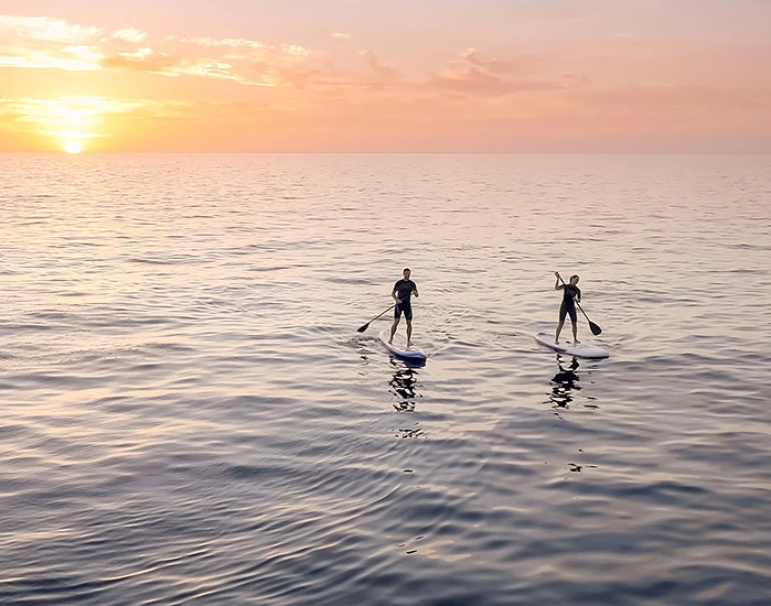 two people paddleboarding at sunset
