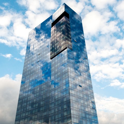 a tall glass building with clouds in the sky
