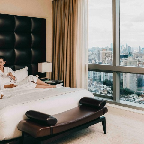 a man sitting on a bed in a hotel room with a large window